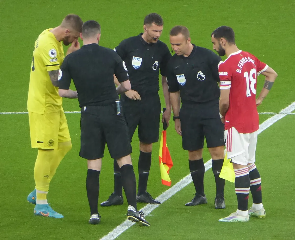 Manchester United captain Bruno Fernandes, wearing the number 18 shirt and captain's armband, stands with the referee, assistant referees and the Brentford goalkeeper at the pre-match coin toss at Old Trafford