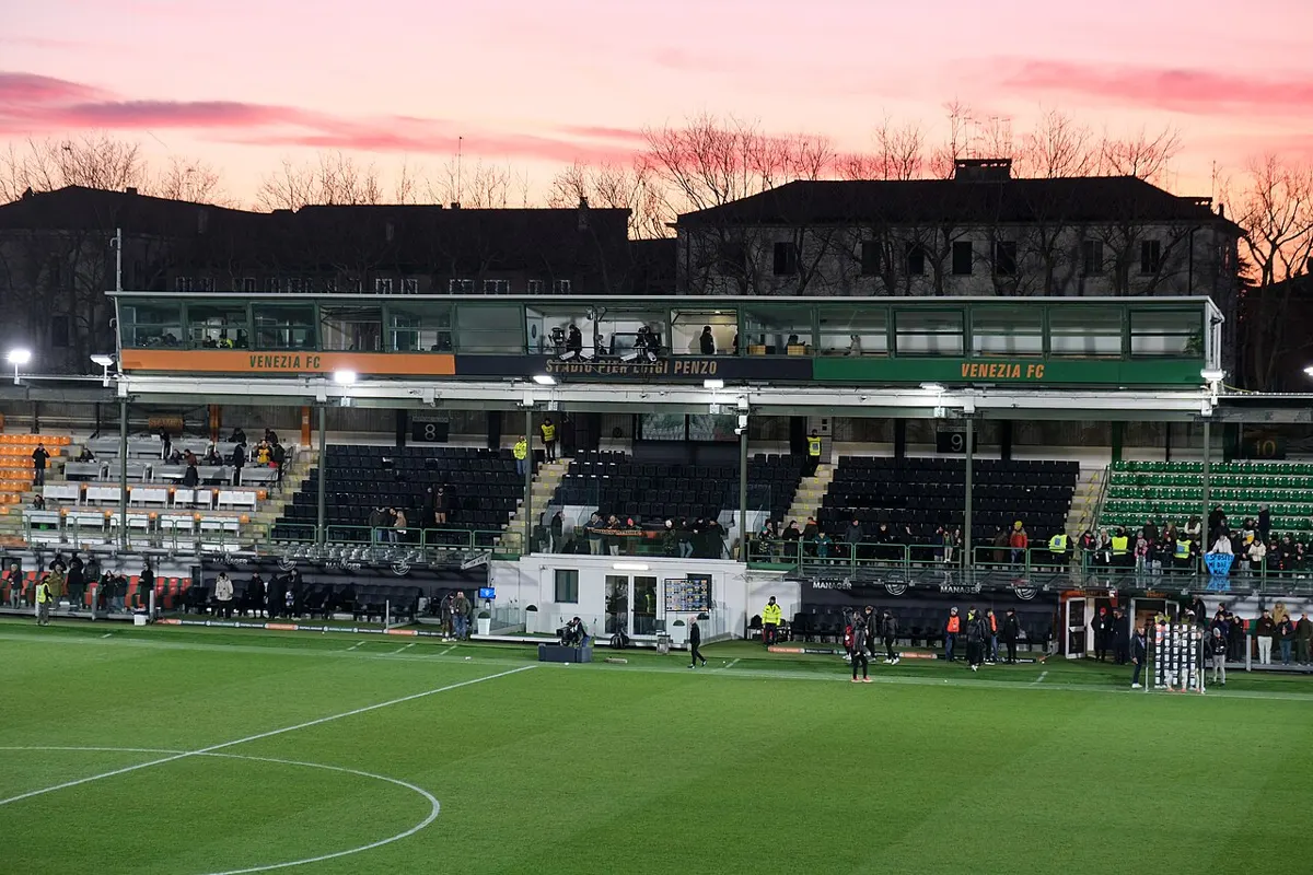 The main stand of the Stadio Pier Luigi Penzo in Venice, with Venezia FC signage, seen from the pitch under a pink evening sky after a Serie A match