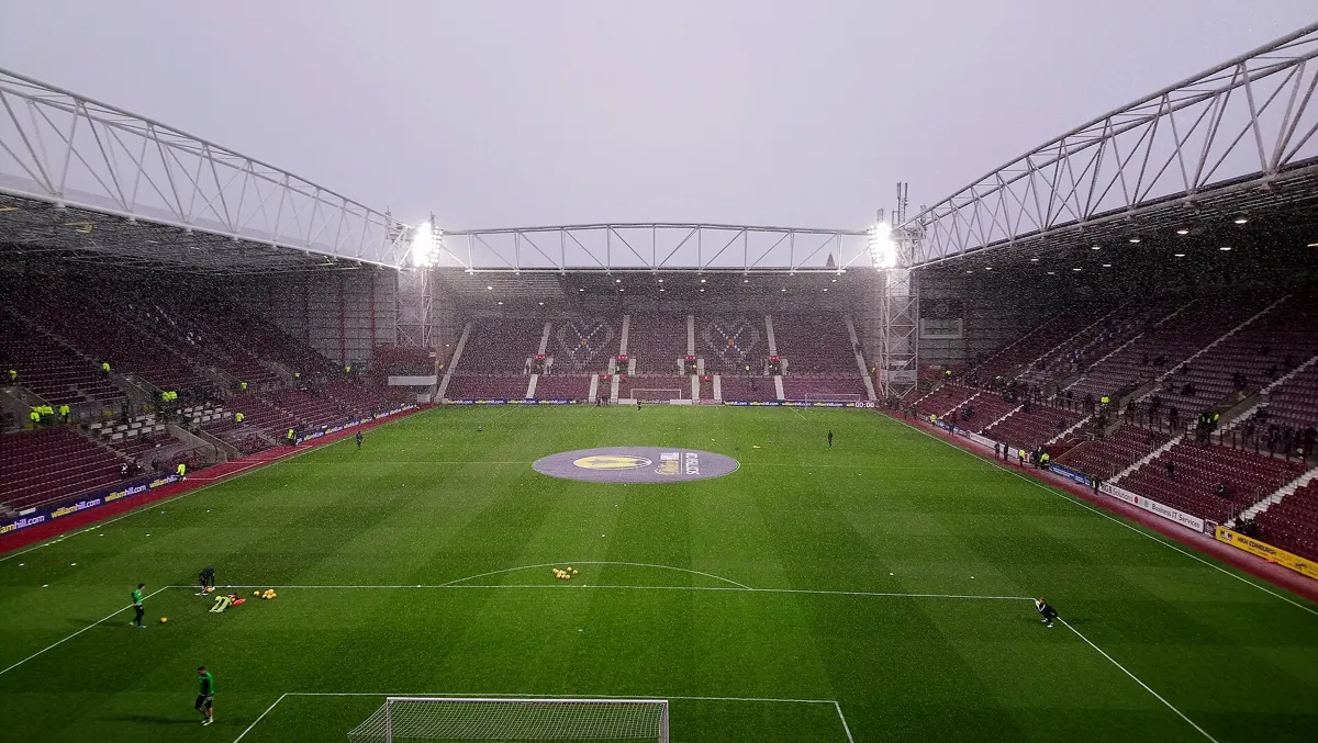 Tynecastle Park, home of Heart of Midlothian in Edinburgh, under floodlights before a match, with maroon seats and players warming up on the pitch