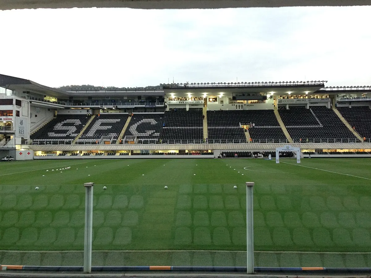 The pitch and main stand at Santos's Vila Belmiro (Estádio Urbano Caldeira) before a Brasileirão match, with black and white seats spelling SFC and footballs laid out for the warm-up